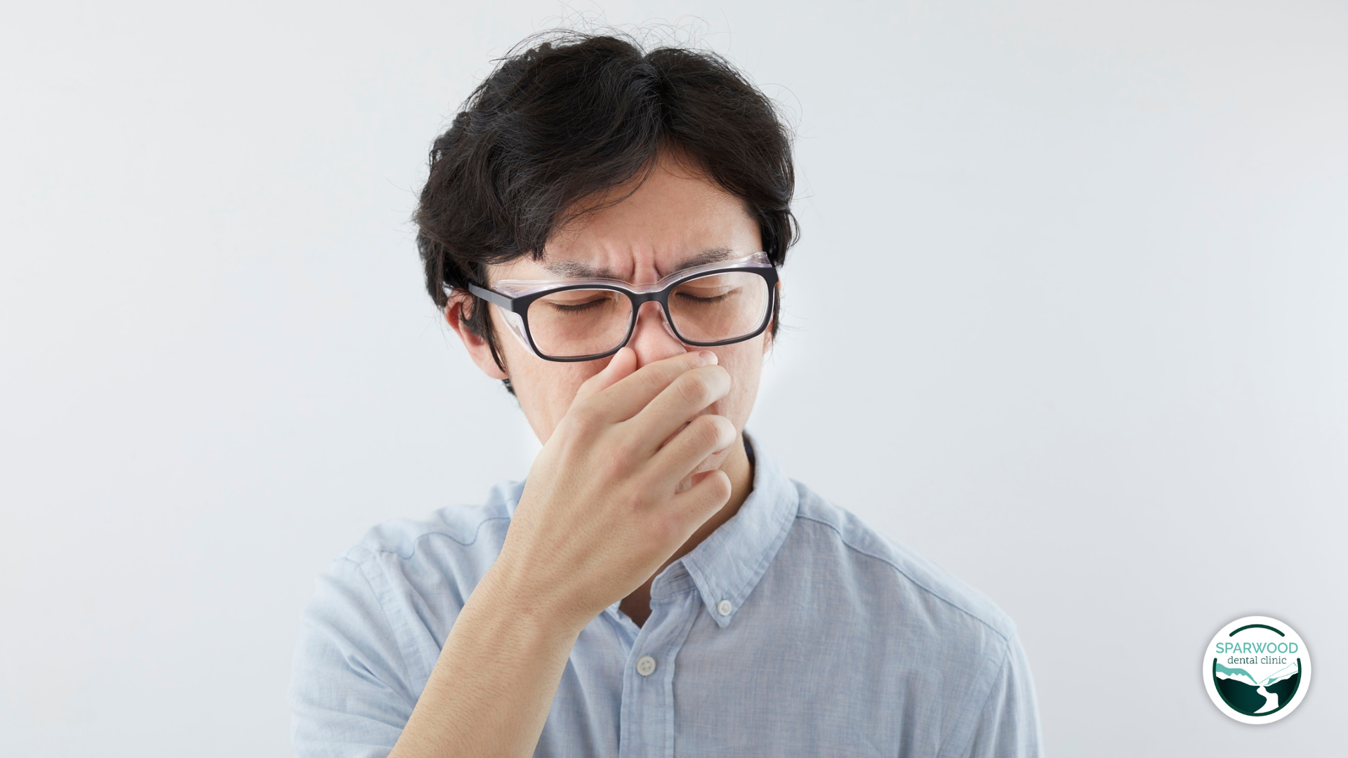Man in glasses pinching his nose, looking uncomfortable against a white background