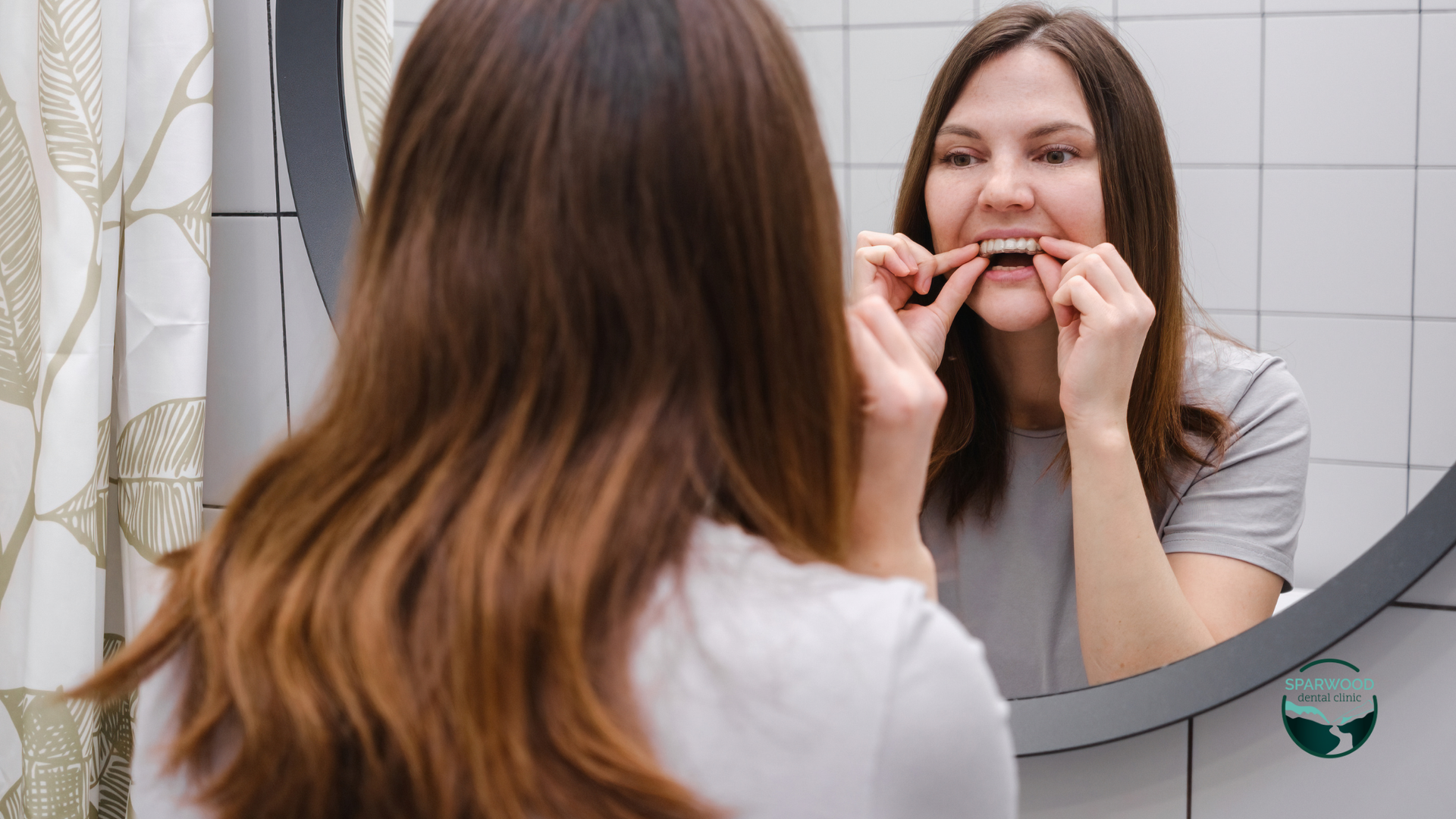 A woman is brushing her teeth in front of a mirror.