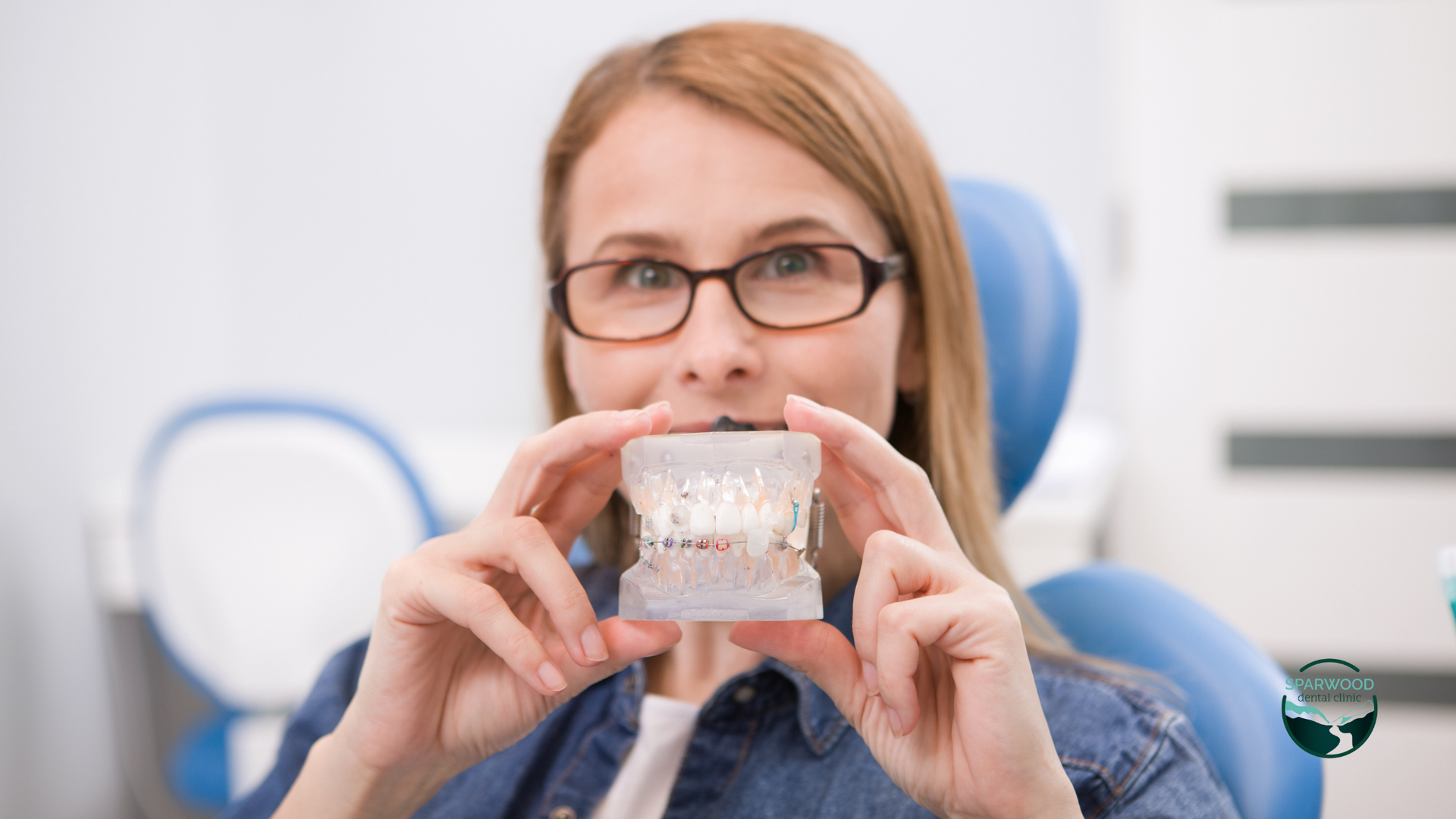 A woman in a dental chair is holding a model of her teeth.