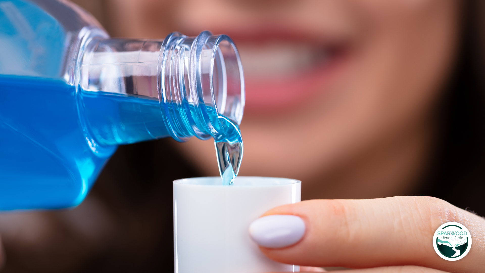 Person pouring blue mouthwash into a white cup, smiling in a well-lit setting.
