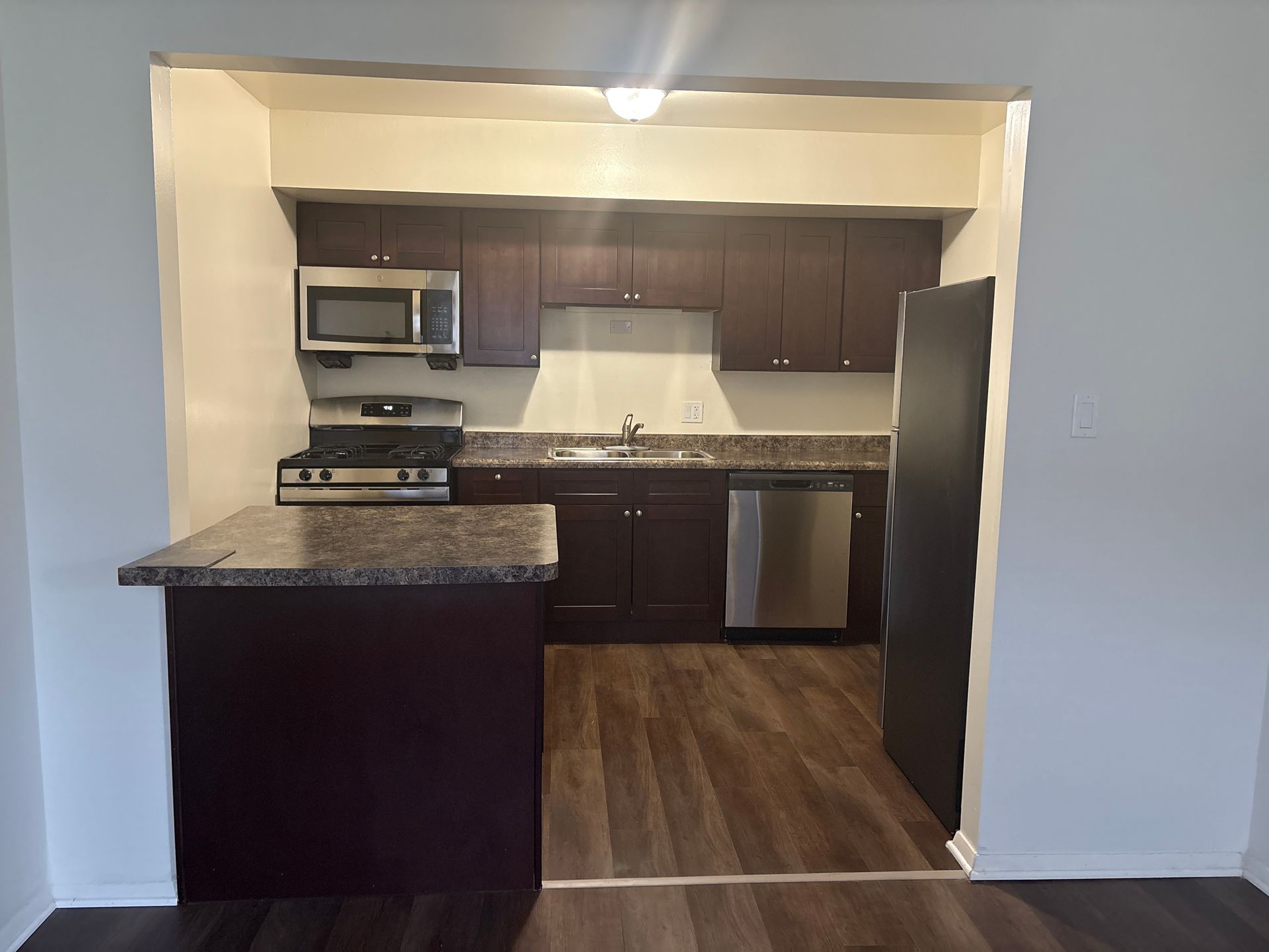 Kitchen with dark cabinets, stainless steel appliances, granite countertops, and a small island.