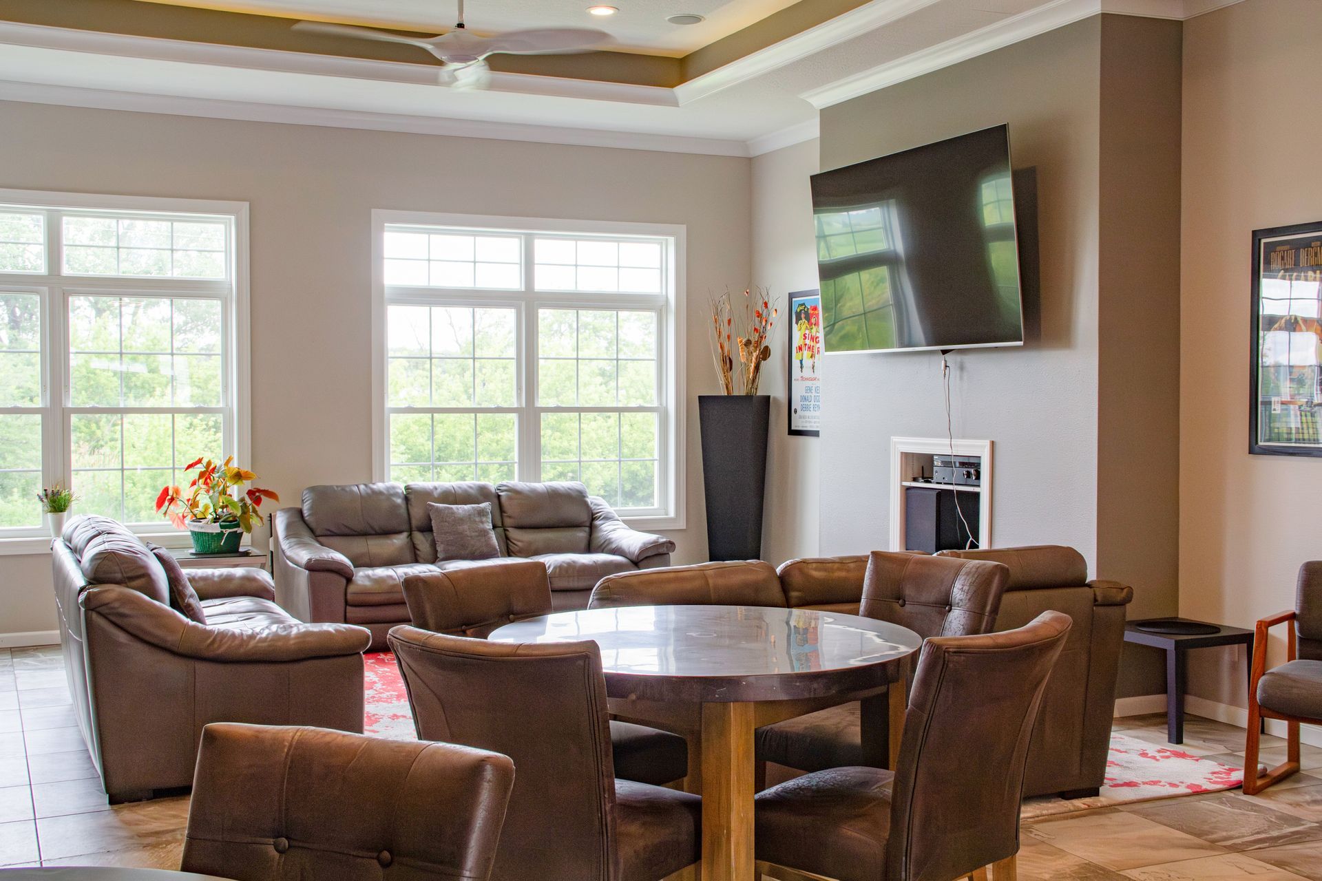 Spacious lounge with leather sofas, round table with chairs, large windows, and a mounted TV.