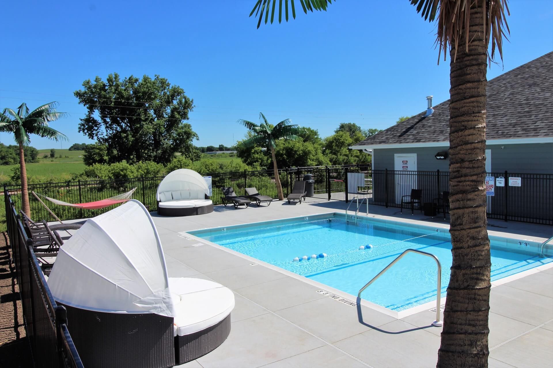 Pool area with blue water, chaise lounges, palm trees, and green fields.