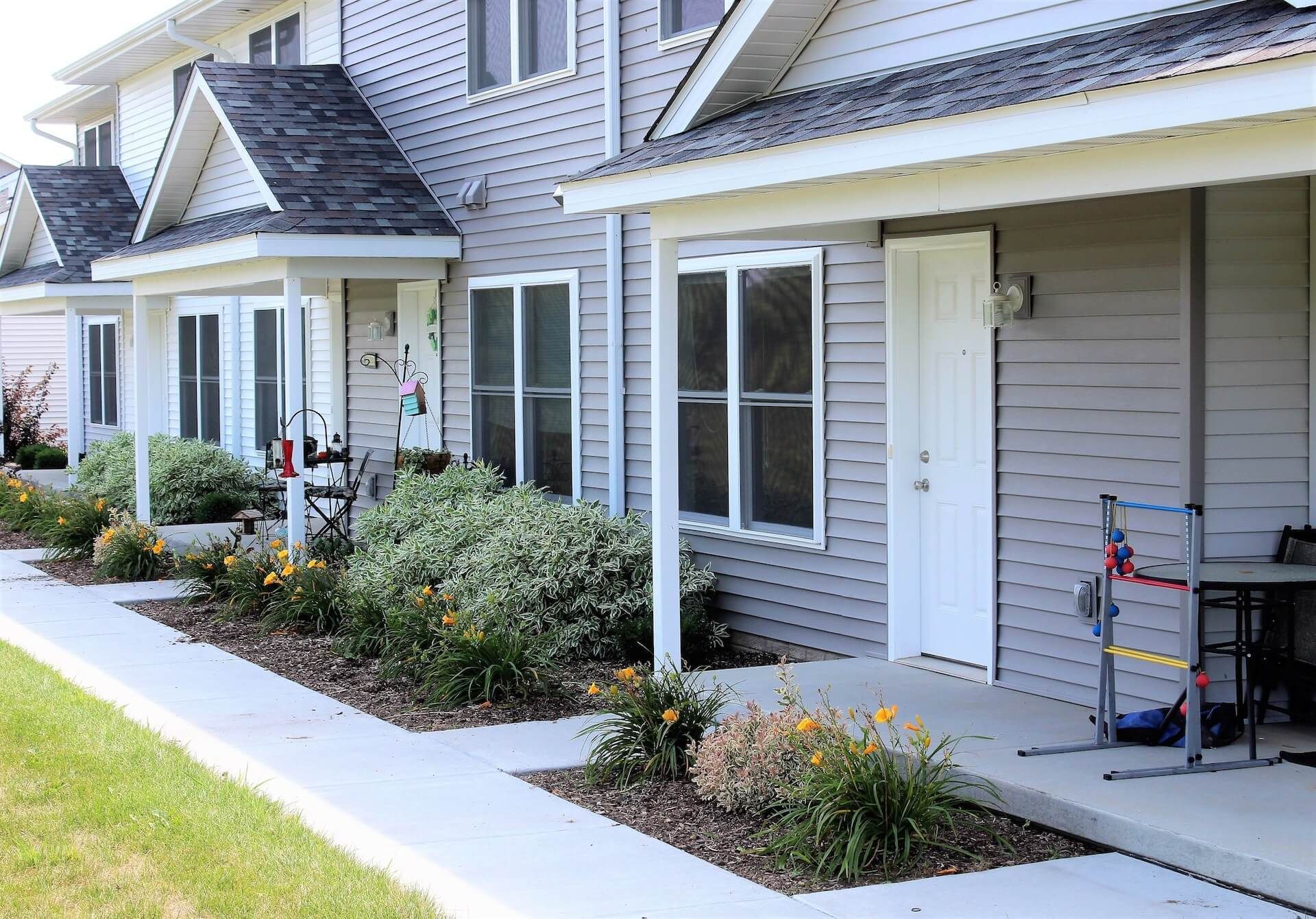 Row of townhouses with white trim, front doors, windows, and small gardens.