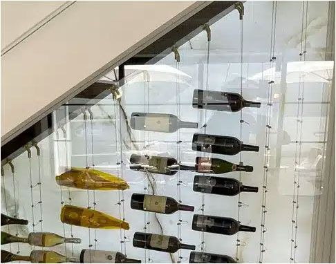 Wine bottles displayed on a stairwell wall, suspended in clear vertical racks