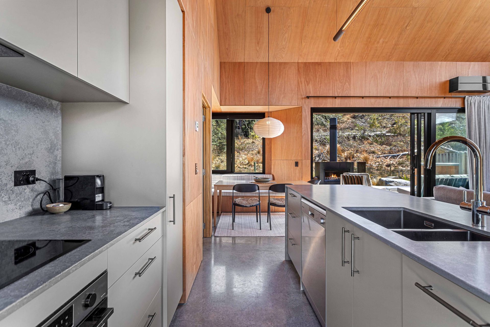 Modern kitchen with wood walls, white cabinets, black countertops, and a view into a dining area.