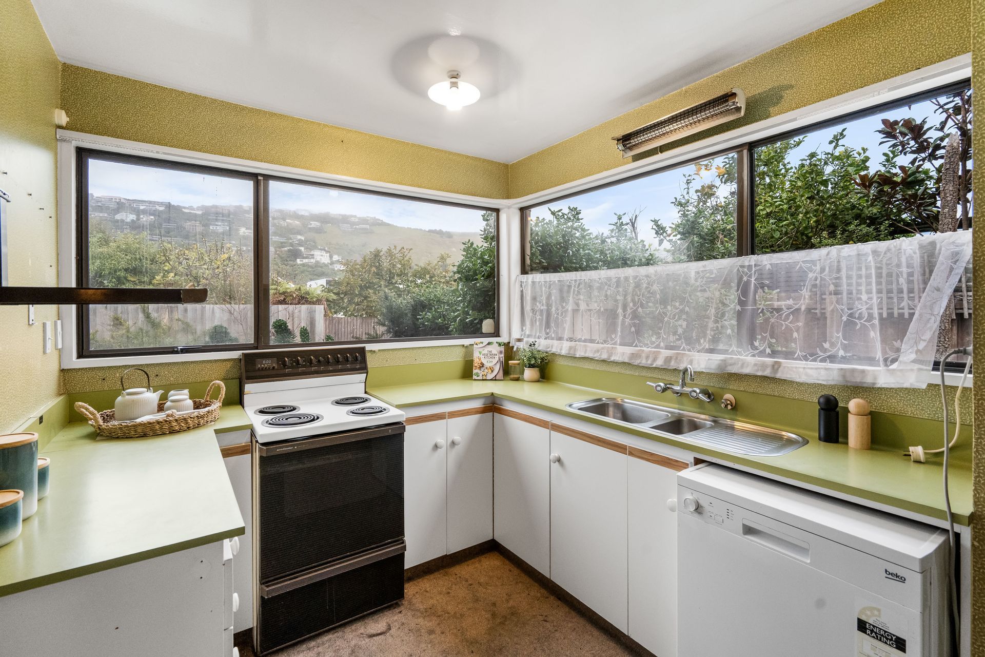 Bright kitchen with yellow walls, large windows, and white appliances overlooking a garden.