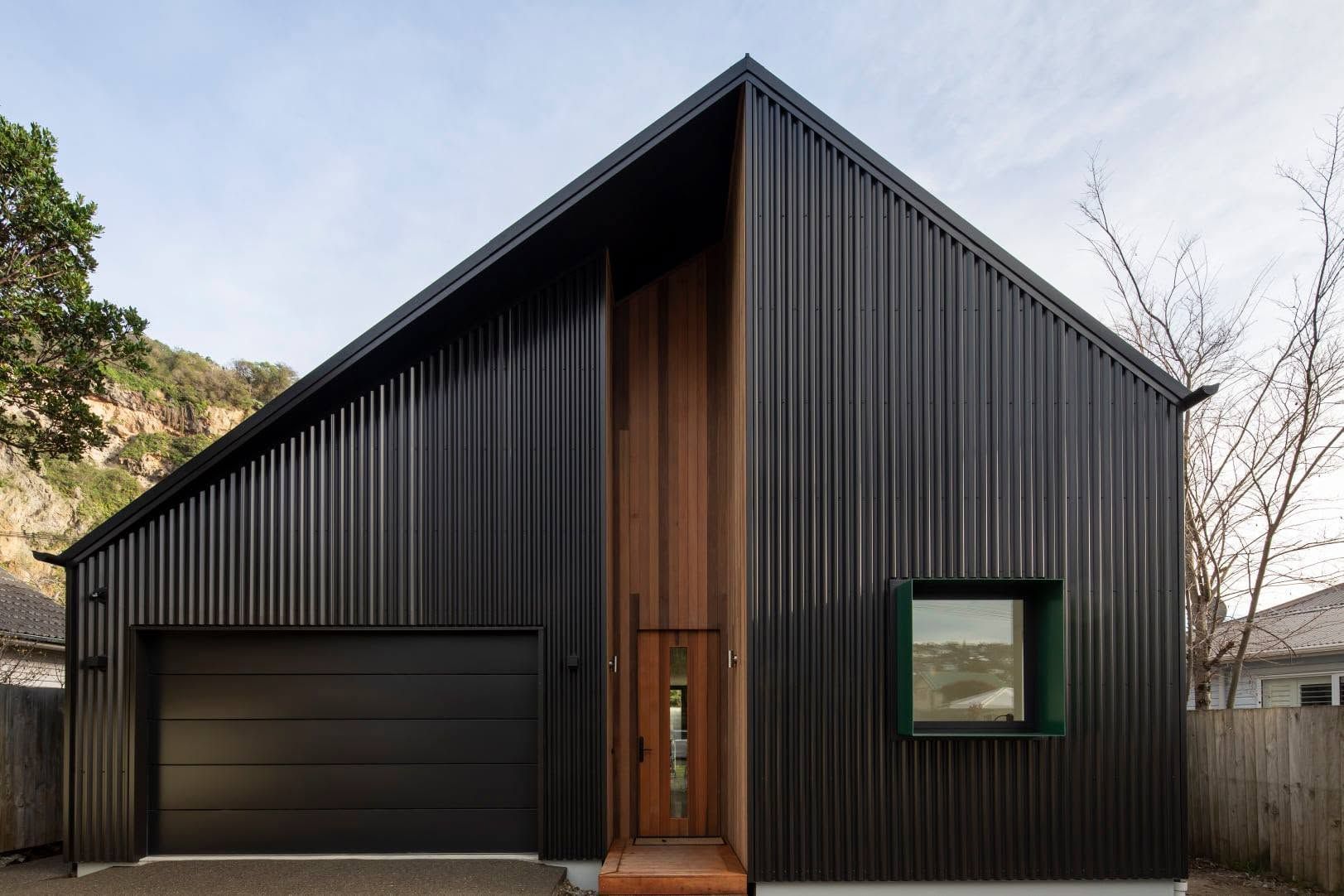 Modern black metal house with a slanted roof, wooden front door, and a small window.