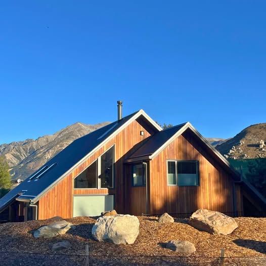 A small wooden cabin with a steep roof in a rocky mountain landscape under a clear blue sky.