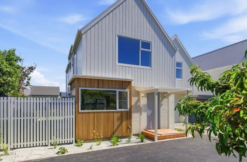Modern white-and-wood house exterior with blue-trim windows, fence, and small front porch