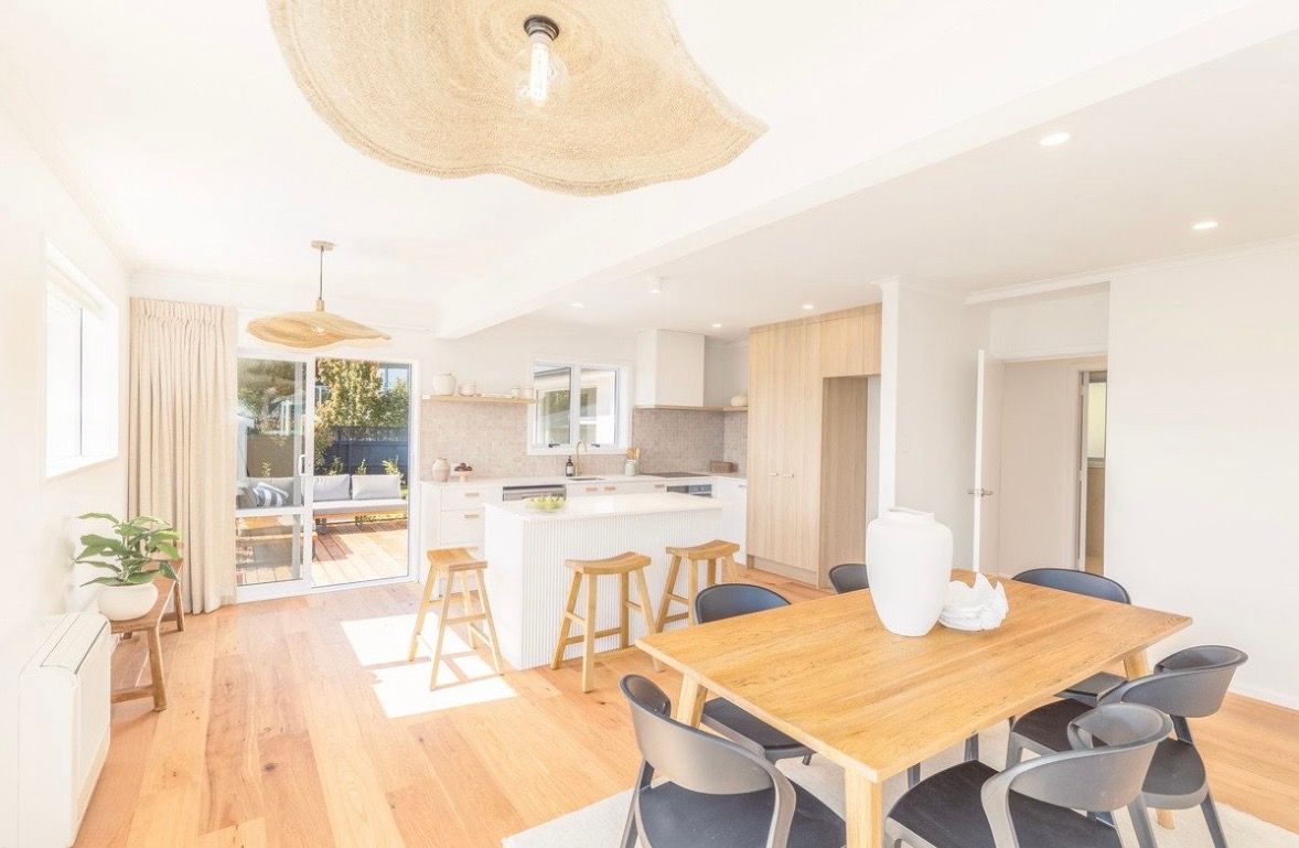 Bright open-plan kitchen and dining room with wood floors, white cabinets, and a wooden table with black chairs.