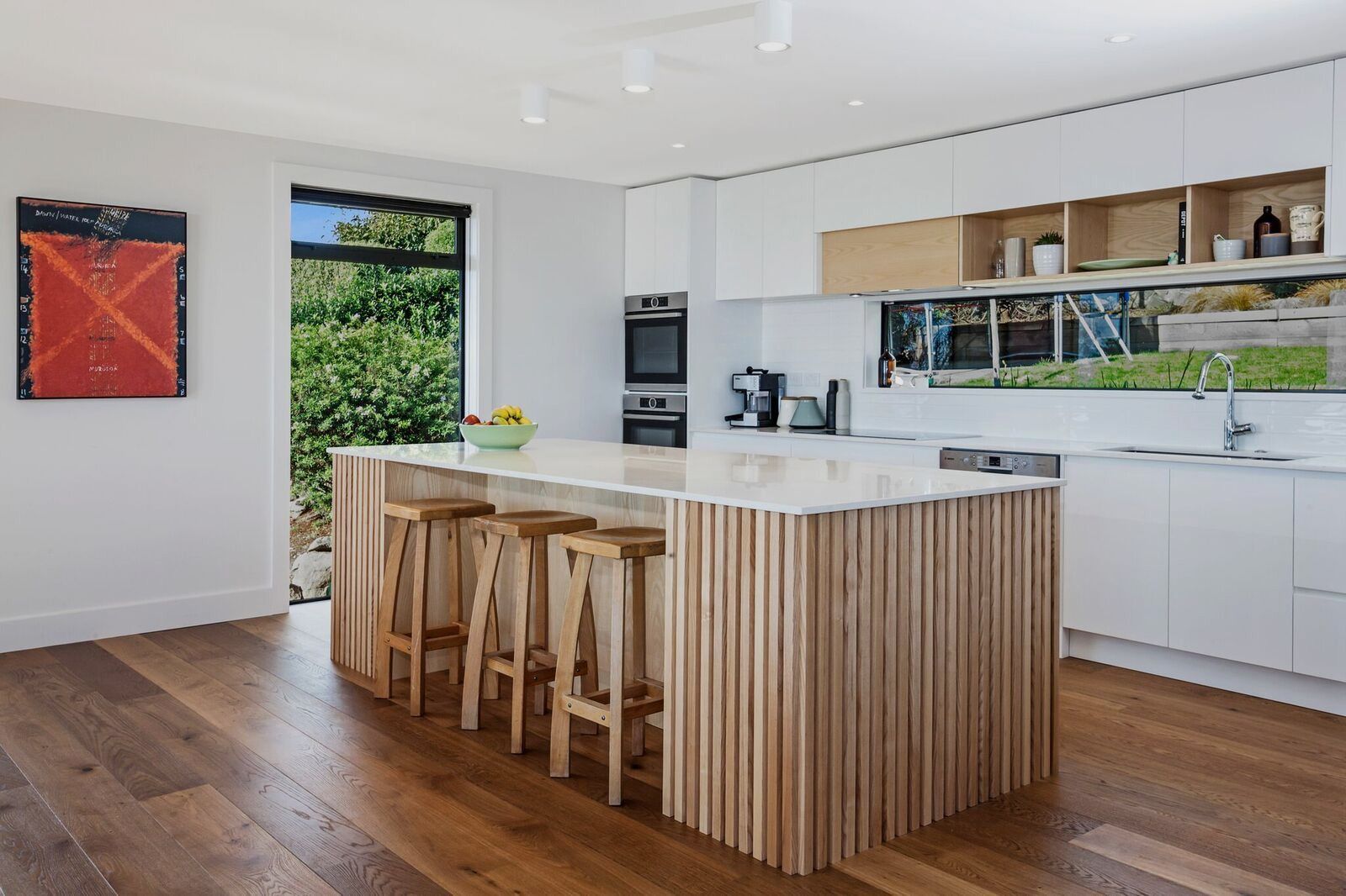 Bright modern kitchen with wood island, bar stools, white cabinets, and large window