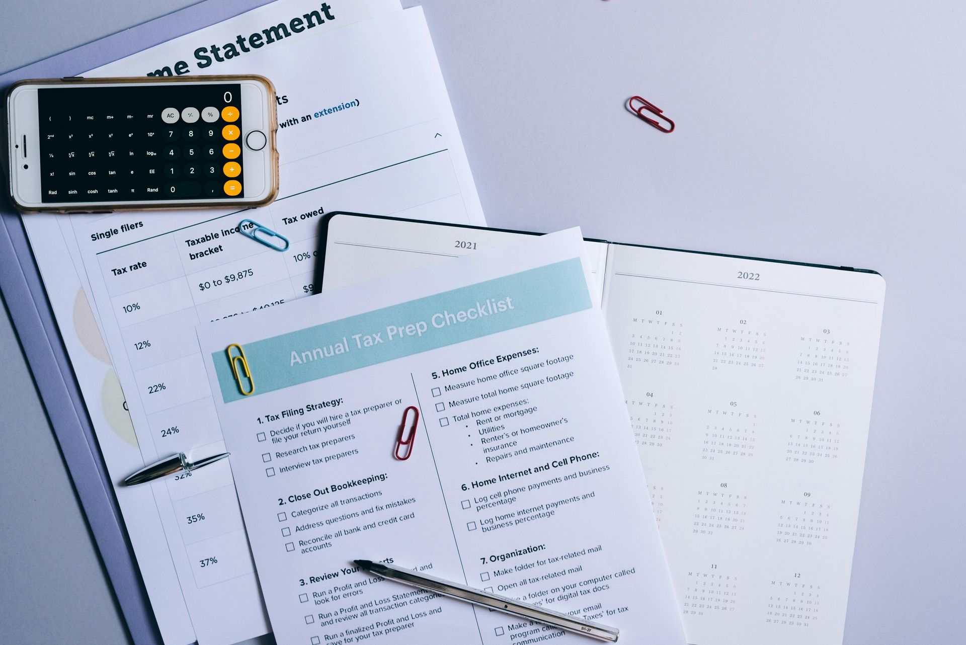 Calculator, pen, and scattered worksheets on a white desk with a turquoise notepad.