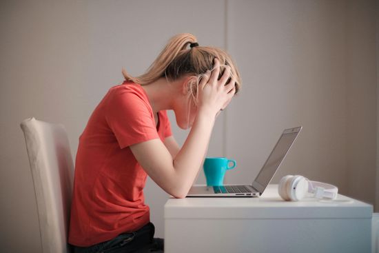 Business owner feeling stuck, sitting at a computer with hands on head. Feeling stuck , needing guidance, needing business coaching.