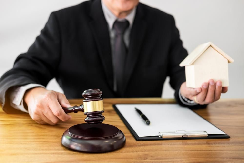 A Judge is Holding a Wooden Gavel and a Model House — All Finanz and Insurance Solutions PtyLtd in Bowen, QLD