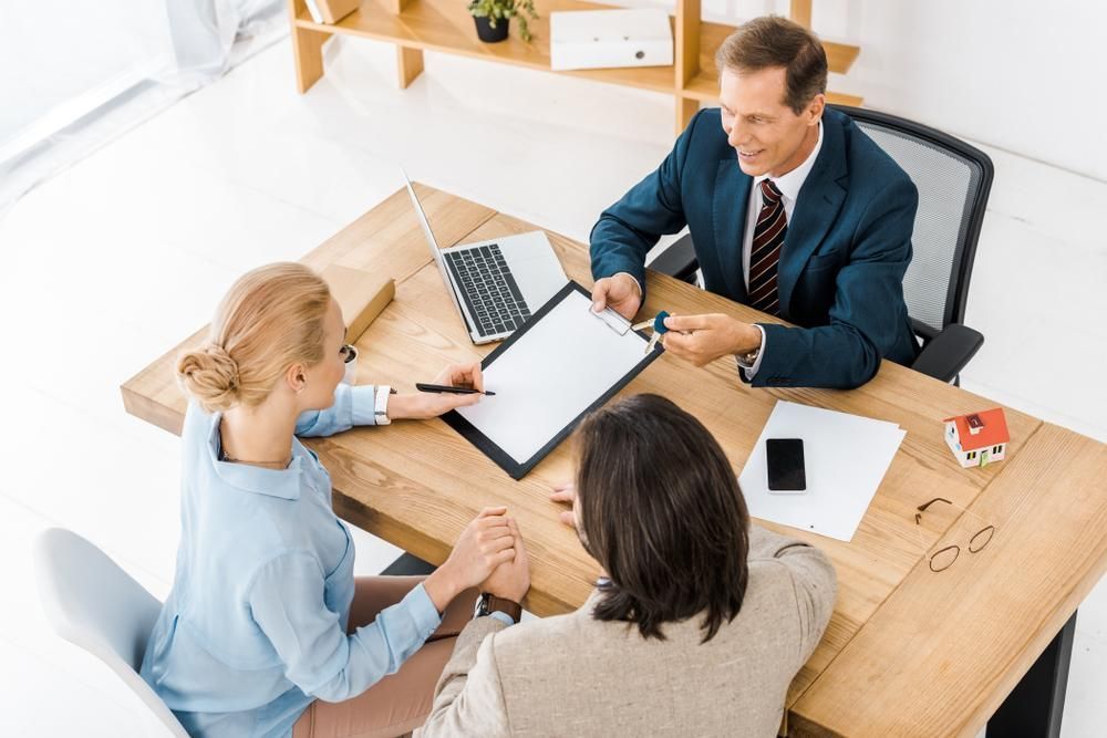 A Man in a Suit and Tie is Sitting at a Table With Two Women — All Finanz and Insurance Solutions PtyLtd in Cannonvale, QLD