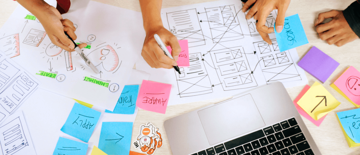 A group of people are sitting at a table with sticky notes and a laptop.