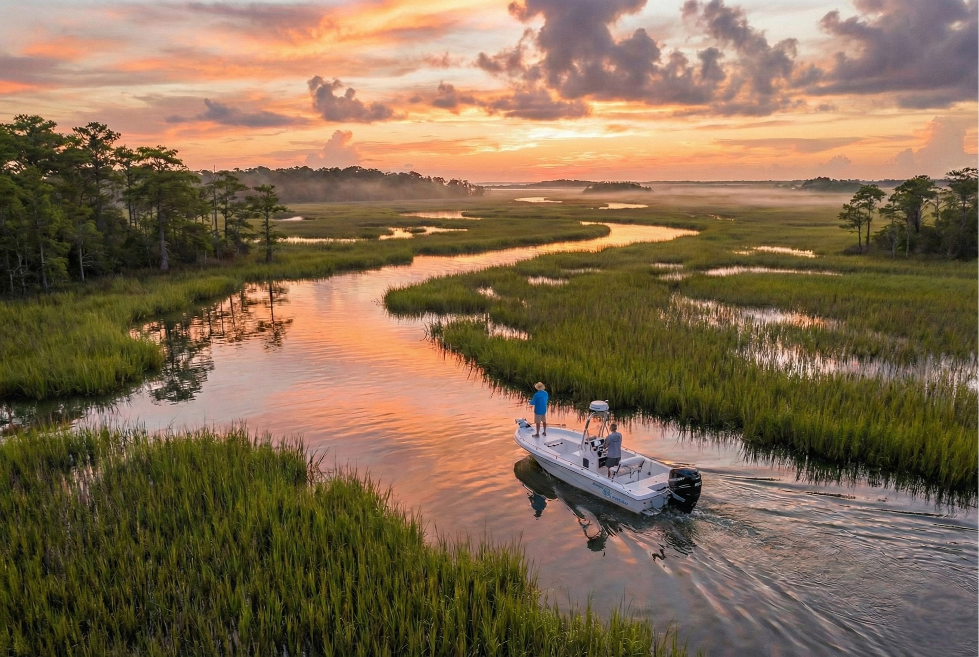 Boat navigating a marshy waterway at sunset; person fishing. Warm colors, sky.