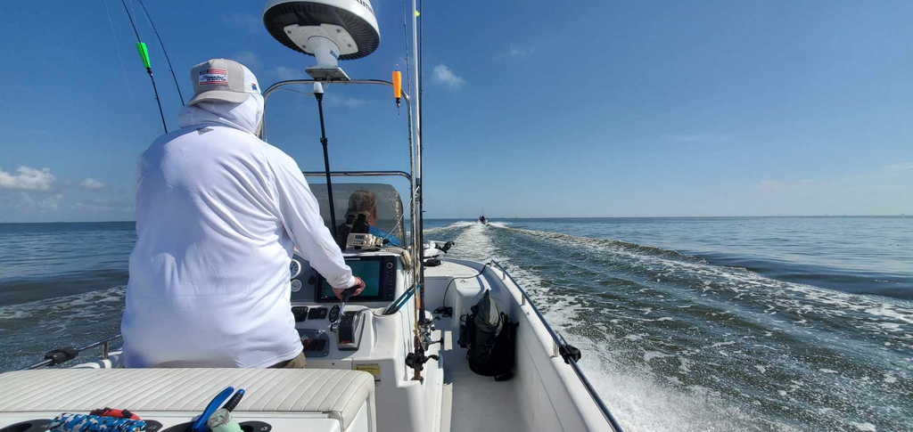 Person driving a boat on a sunny day. The boat is creating a wake.