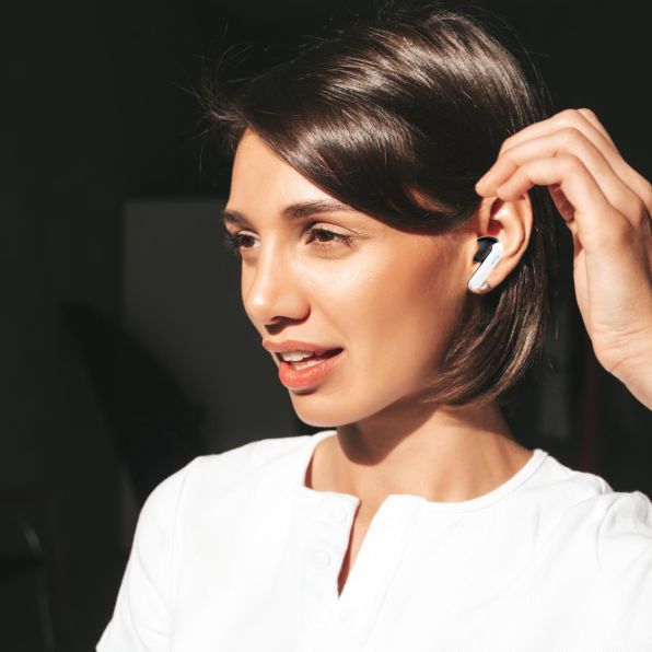 Woman in a white top adjusting a wireless earbud in warm sunlight