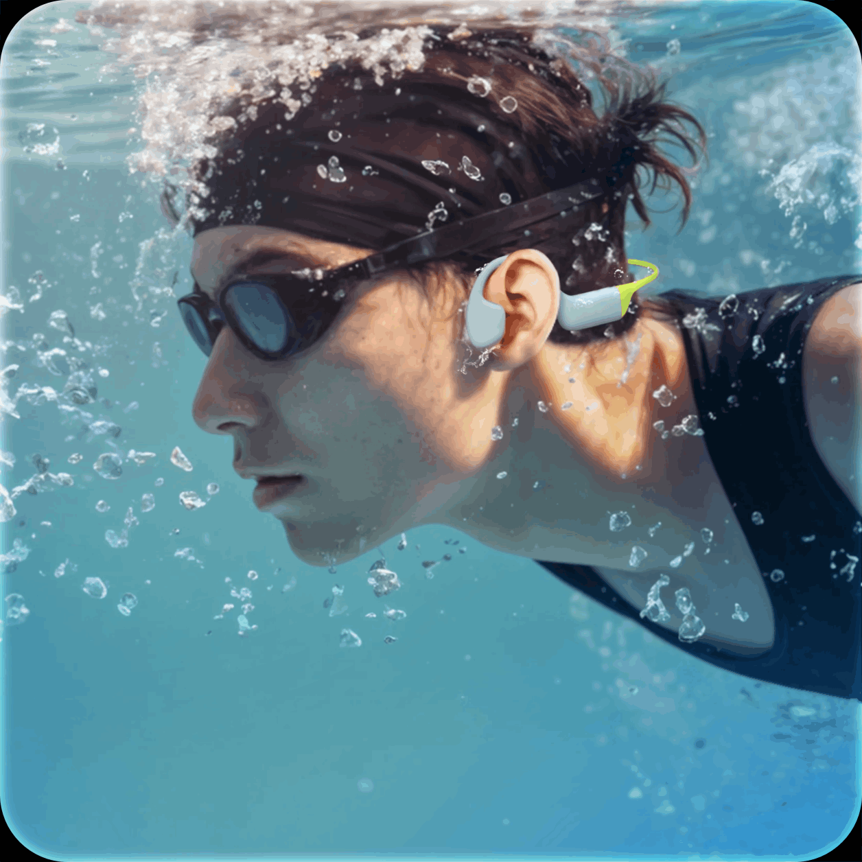 Swimmer wearing goggles and earplugs underwater, swimming through clear blue water