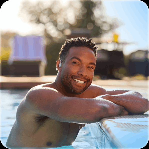 Person smiling while leaning on the edge of a swimming pool outdoors