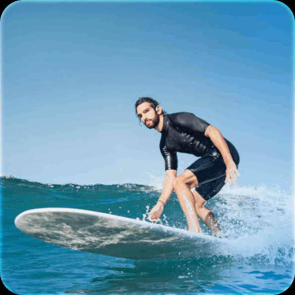 Surfer riding a wave on a white surfboard under a clear blue sky