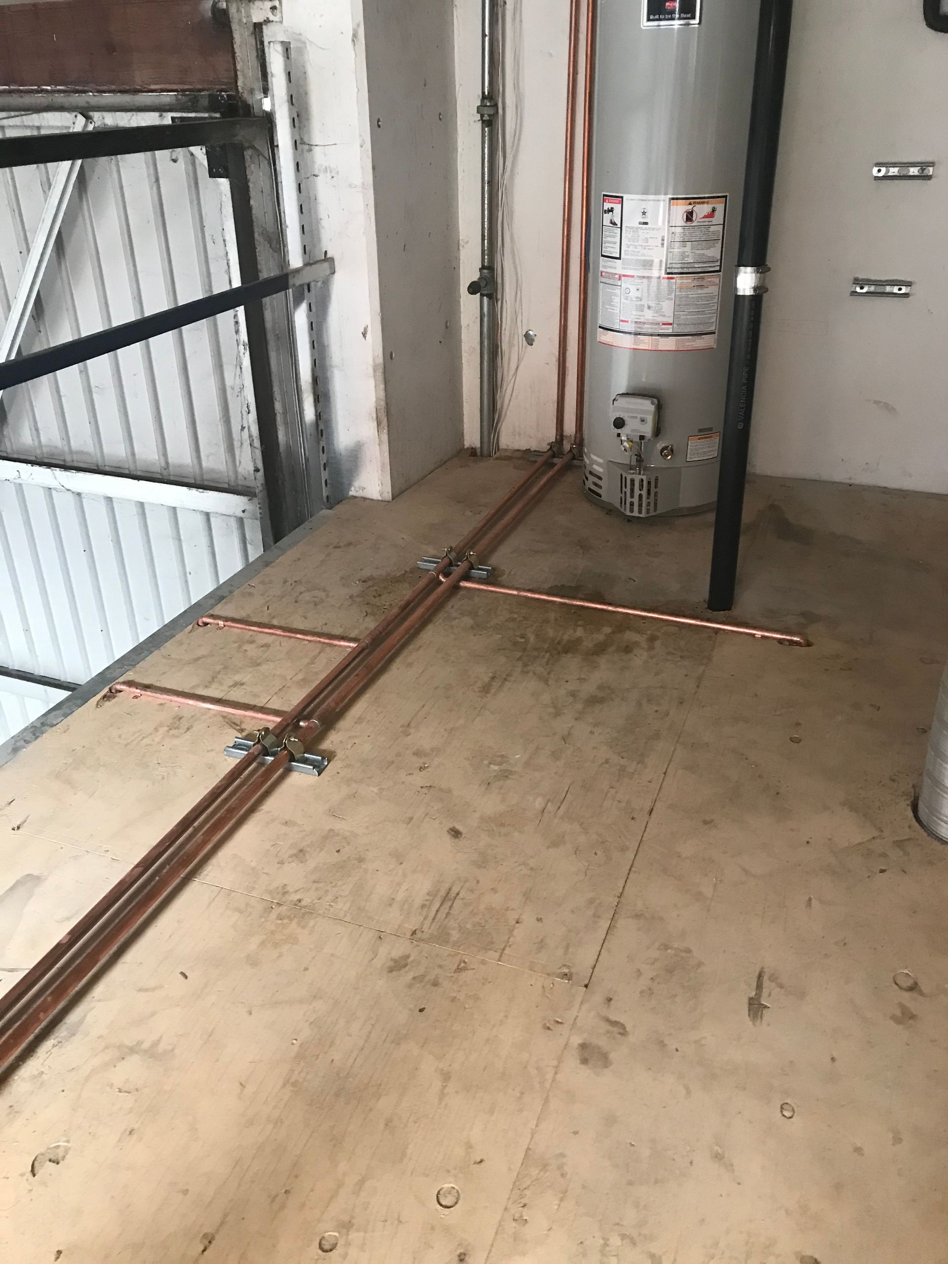 A water heater is sitting on a wooden floor in a garage.