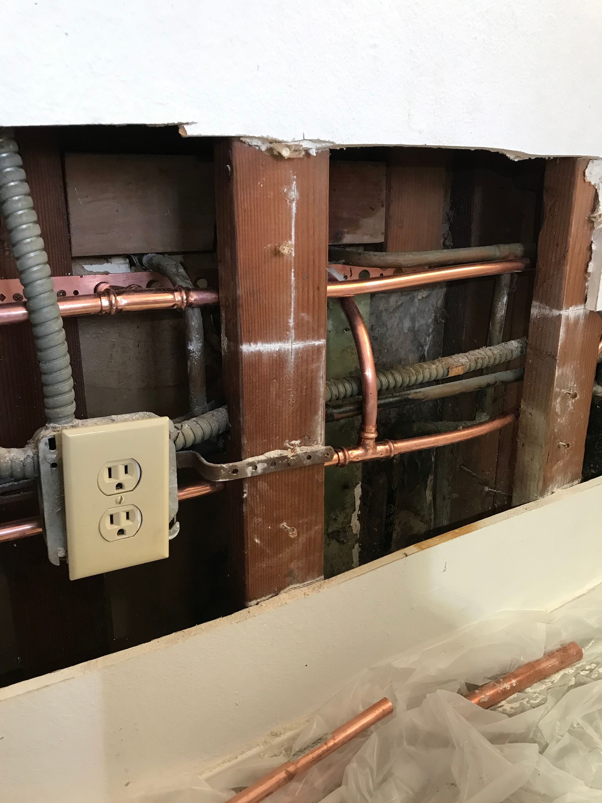 A close up of a wall with a socket and copper pipes.