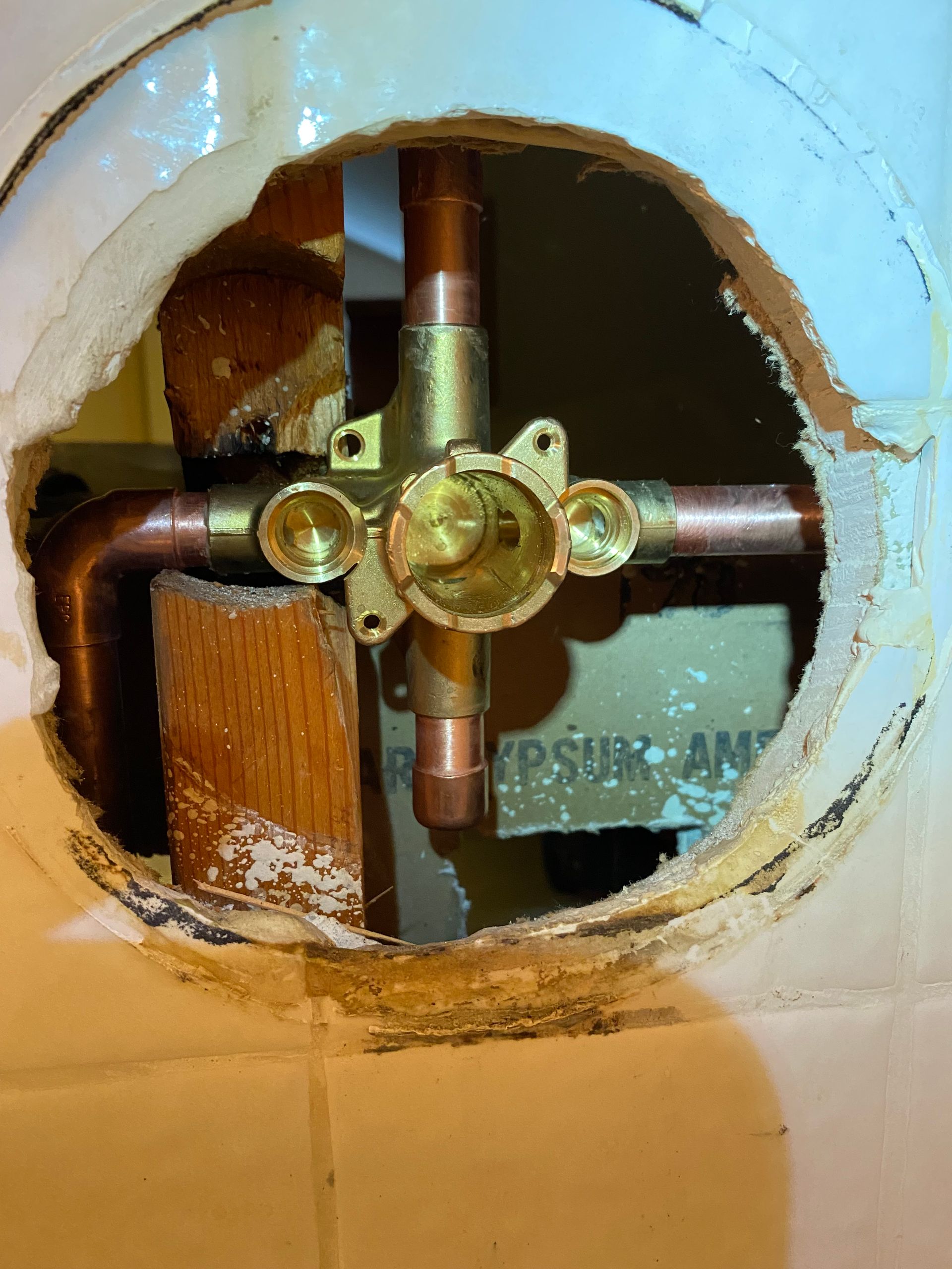 A hole in a wall with copper pipes coming out of it.