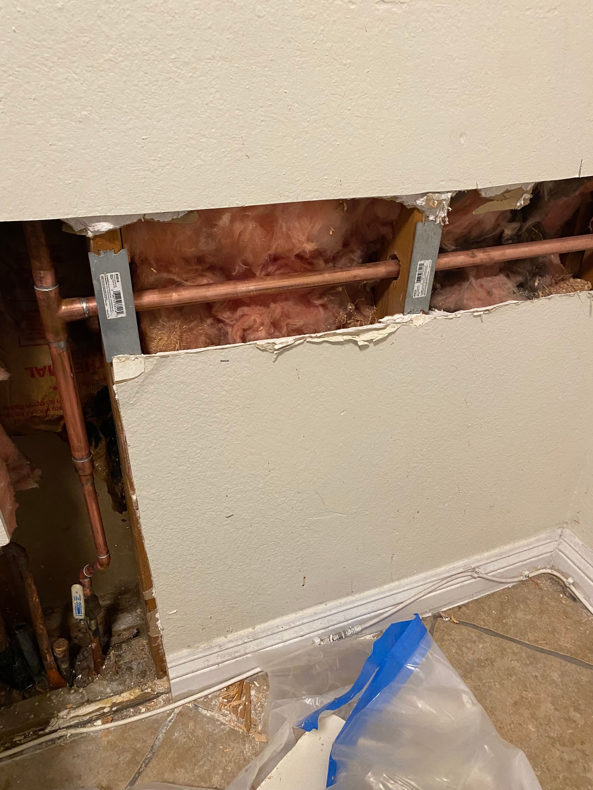 There is a hole in the wall with copper pipes coming out of it.