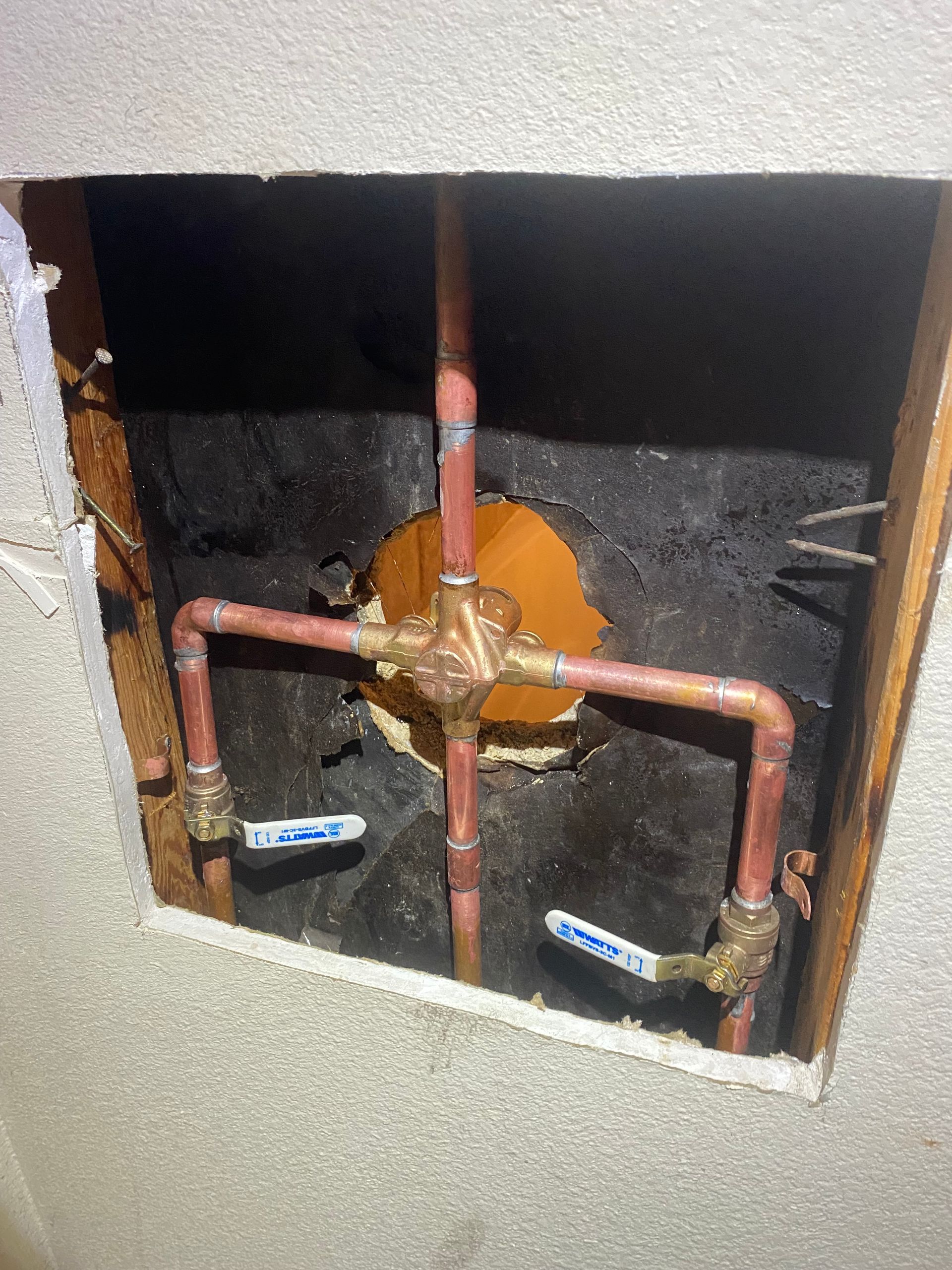 A hole in a wall with copper pipes coming out of it.