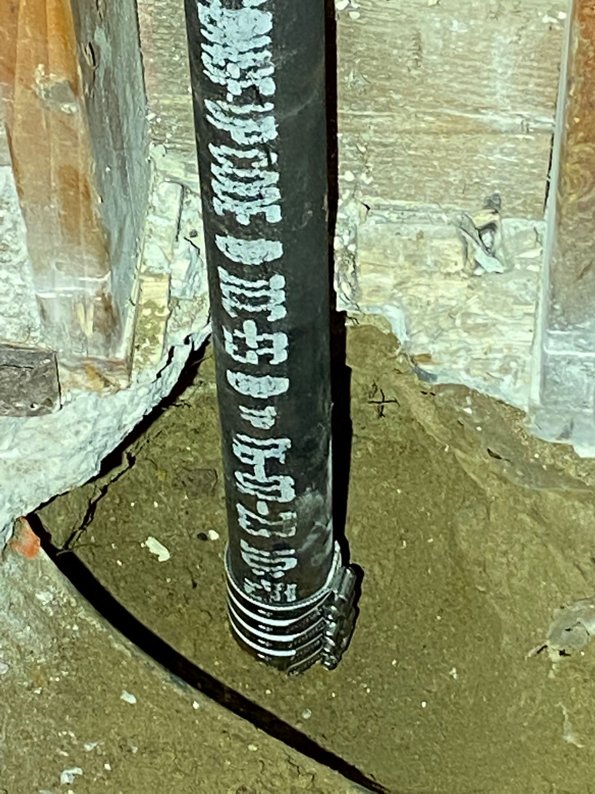 A black pipe with chinese writing on it is sitting in the dirt.