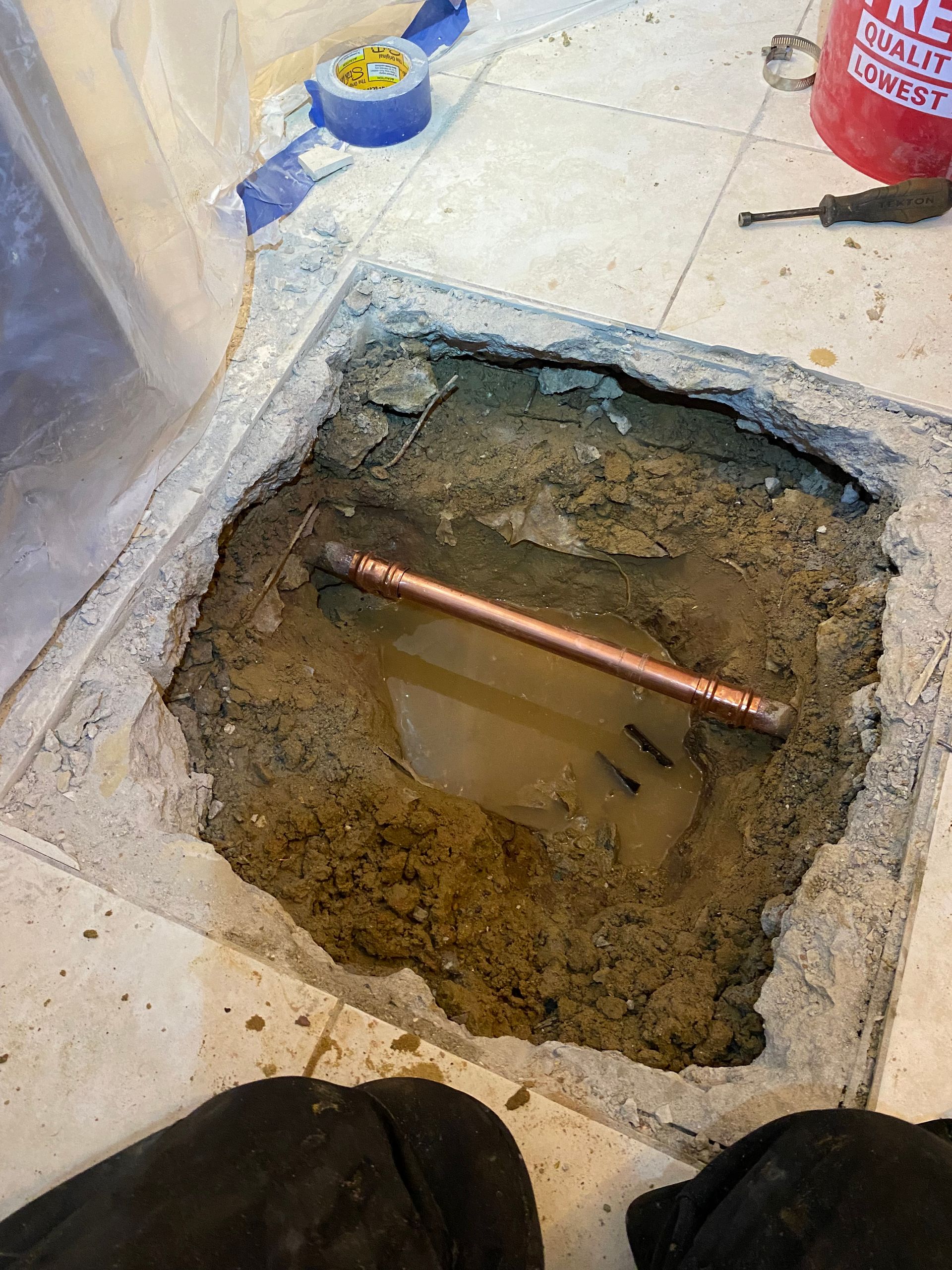 A hole in the floor with a copper pipe in it.