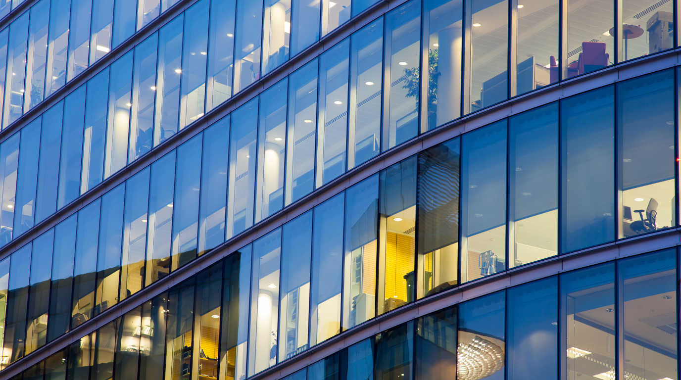 Modern glass office building with illuminated windows reflecting the surrounding city skyline.