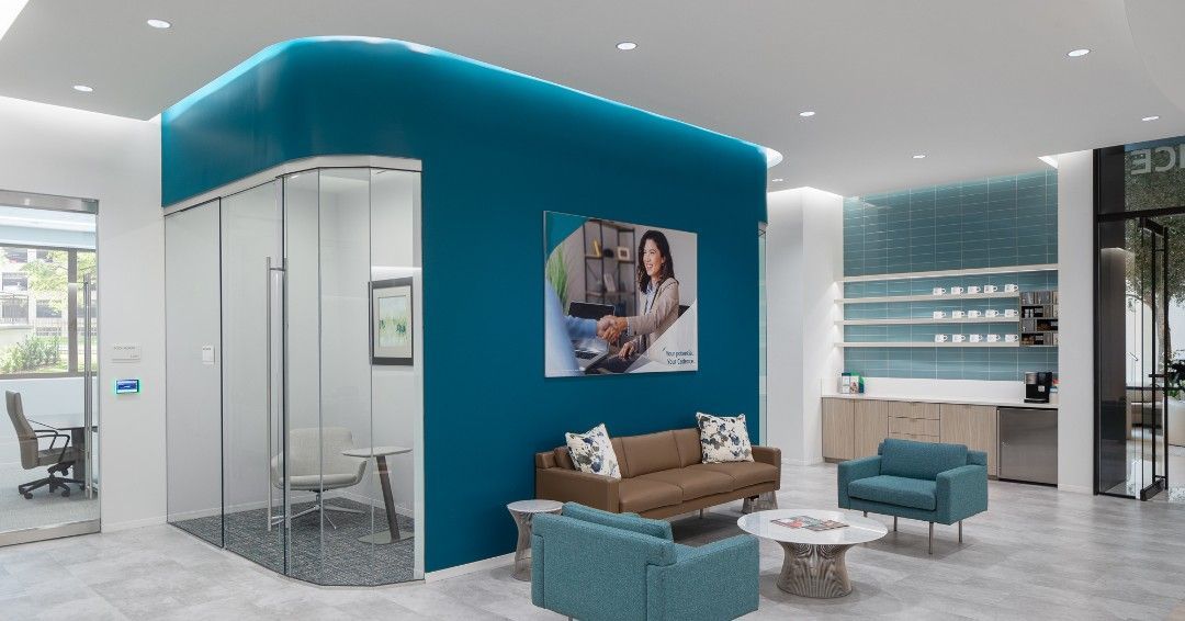 Modern office reception area with teal accent wall, seating, and glass-walled private office.