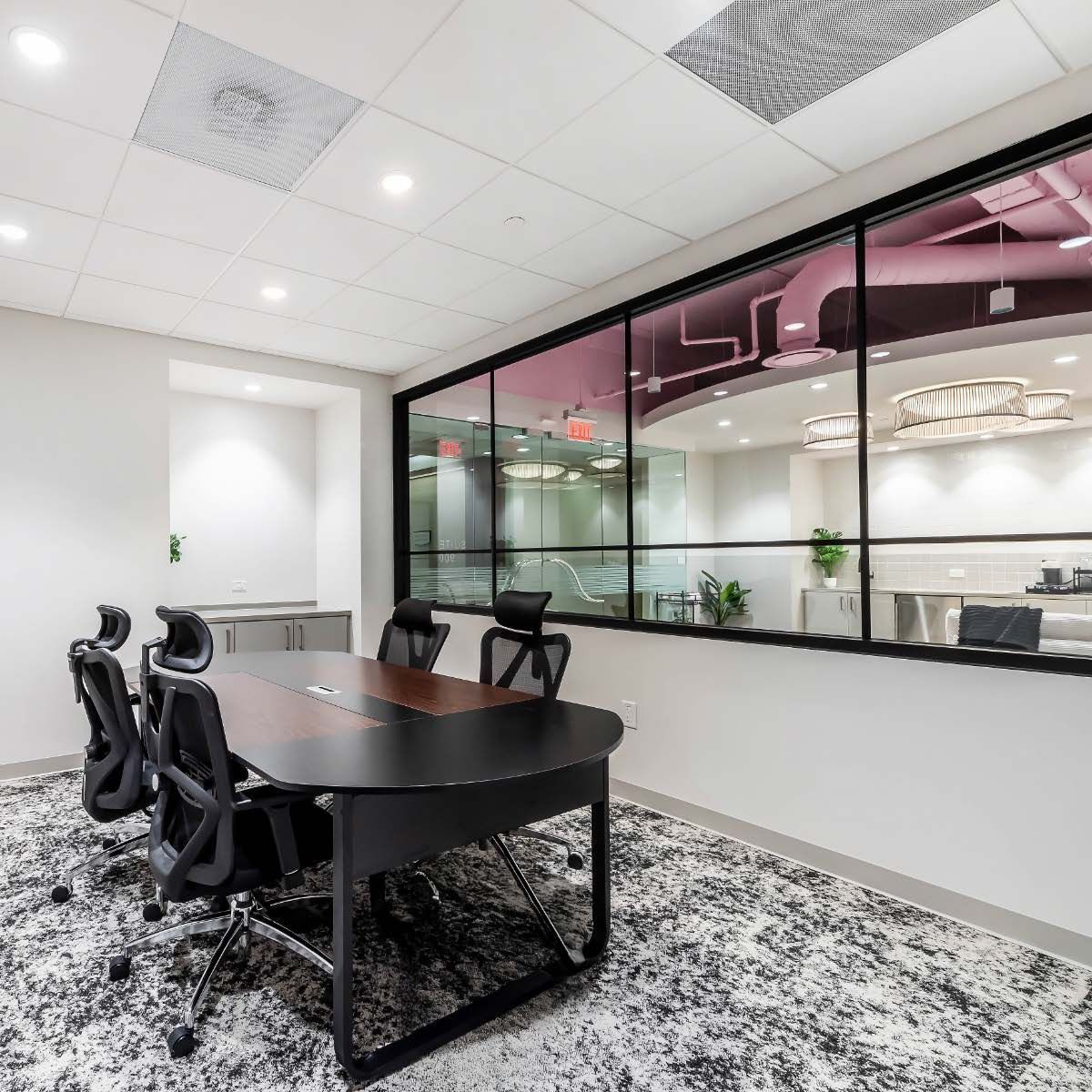 Conference room with oval table, black chairs, and large window overlooking another room.