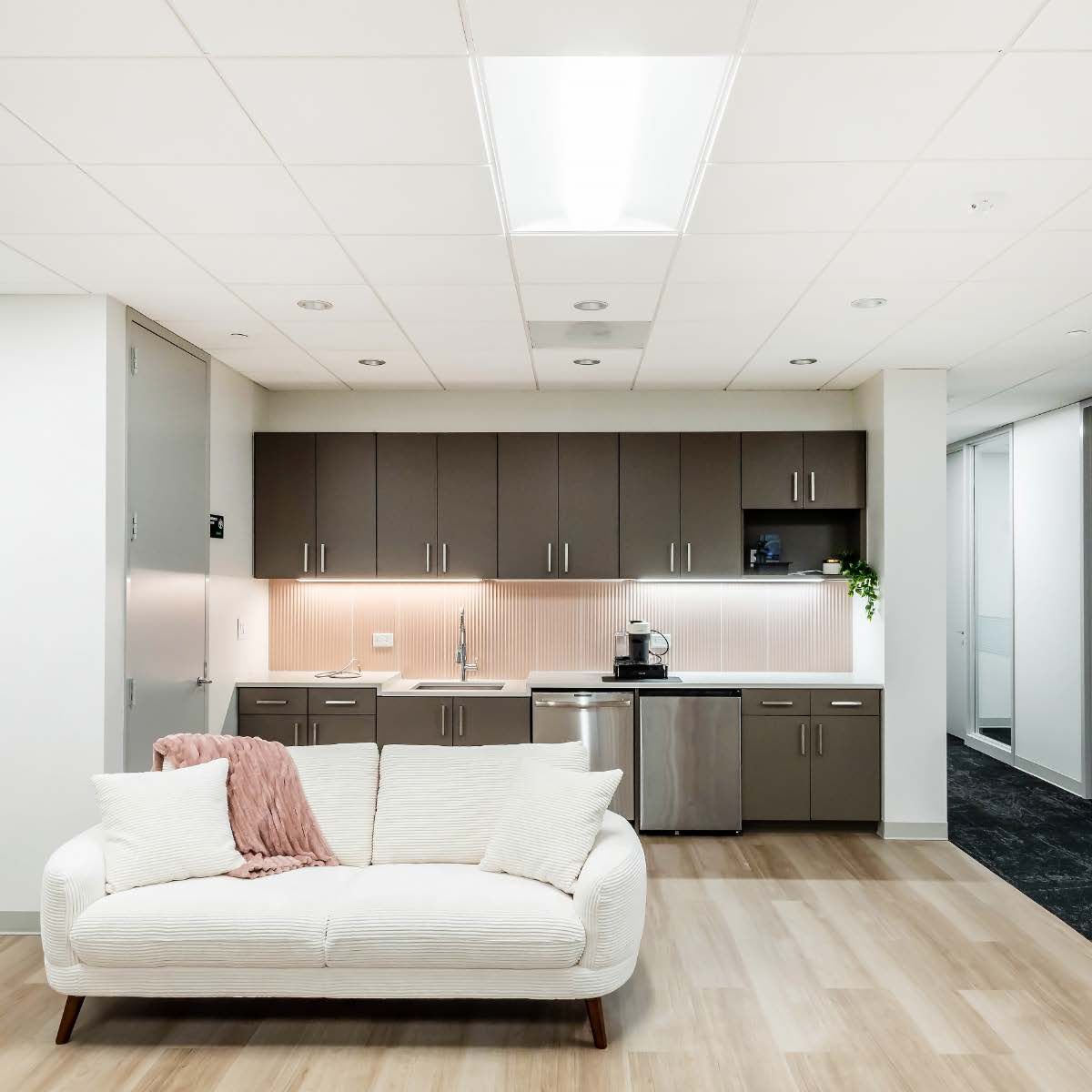 Lounge area with white sofa, kitchenette with dark cabinets, and light wood flooring.