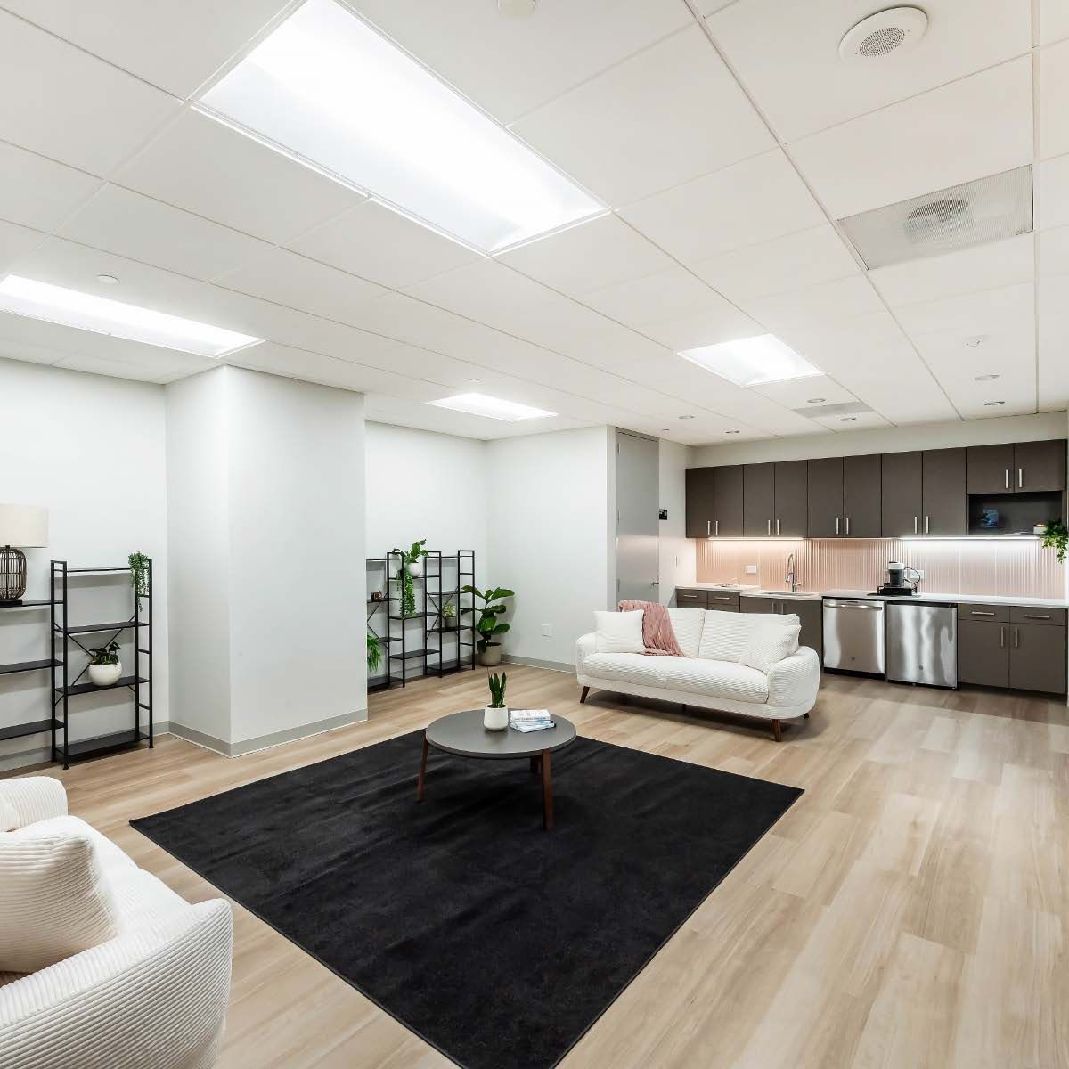 Modern office lounge with white sofas, black rug, and kitchen.