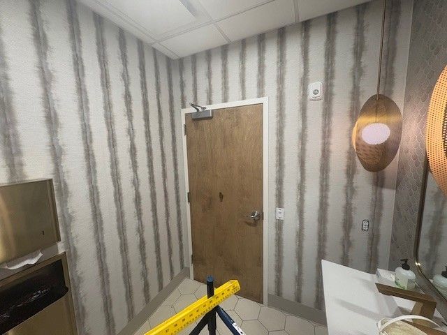 Small bathroom with vertical striped wallpaper, wooden door, and a vanity on the right.