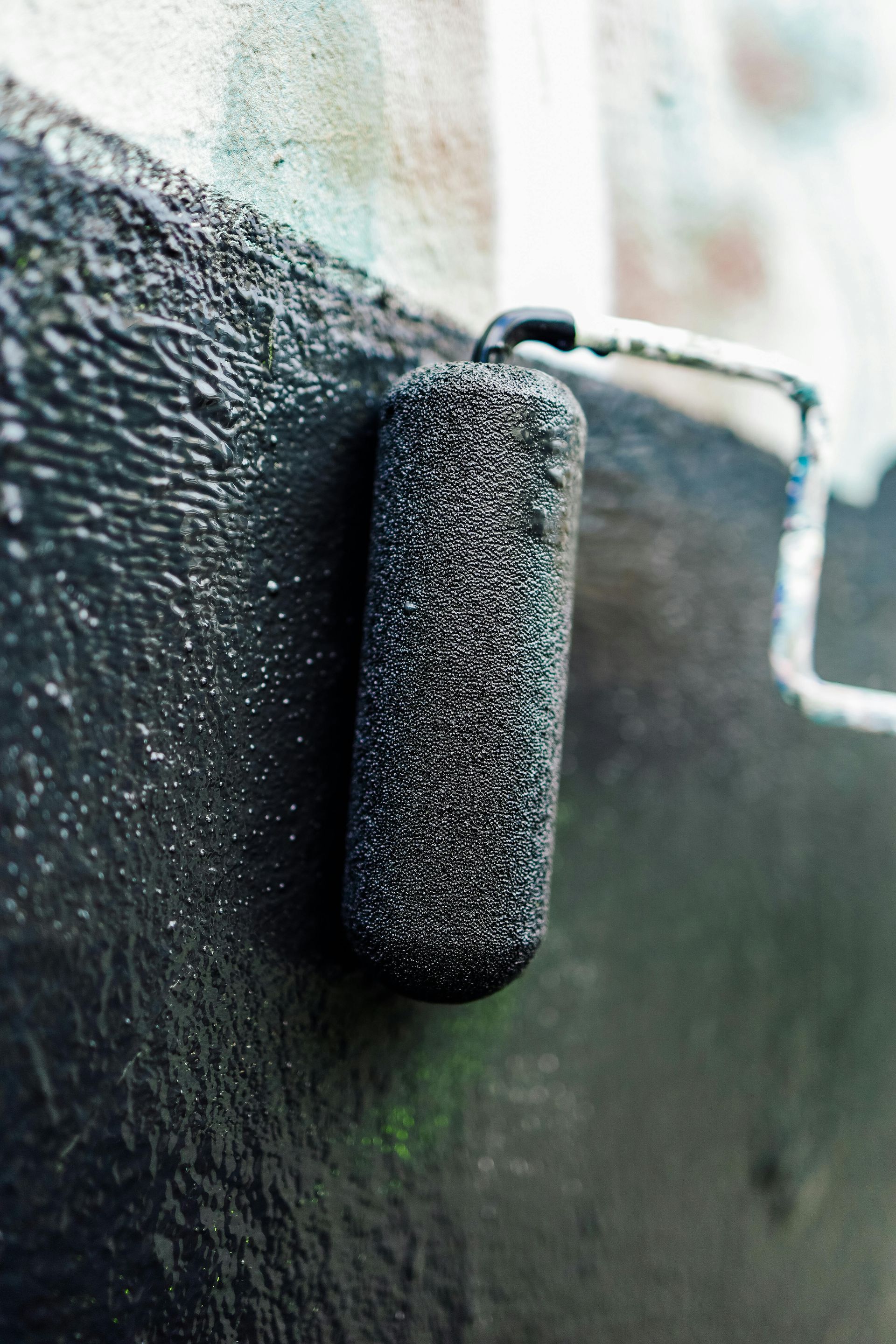 Paint roller applying black paint to a wall.