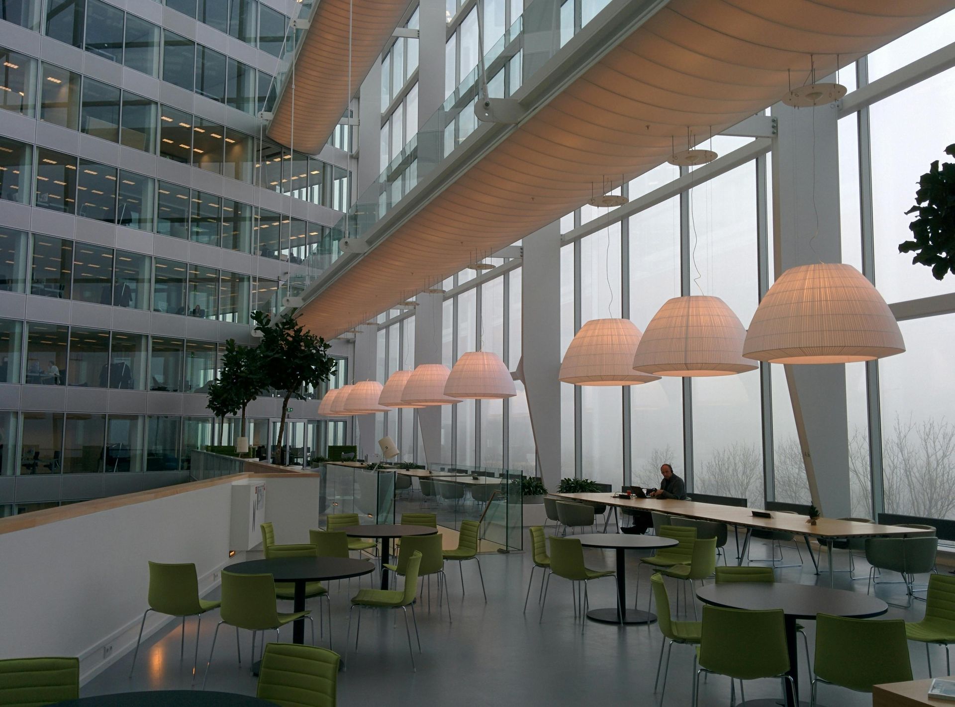 Interior of a modern building with a seating area, large windows, and pendant lights.