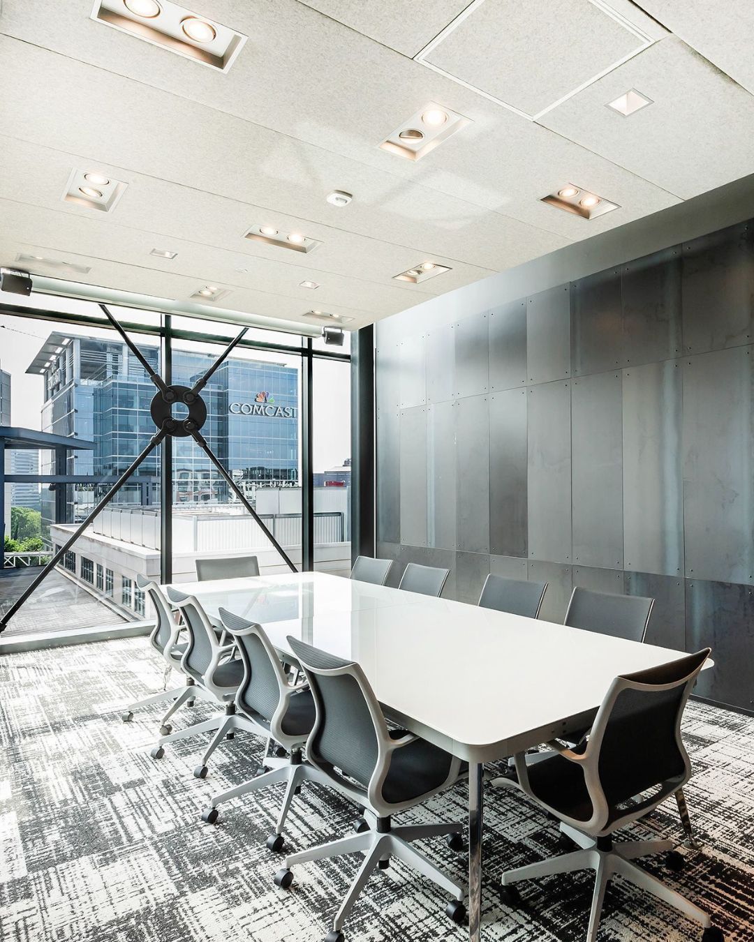 Conference room with white table and black chairs, large window with cityscape view.