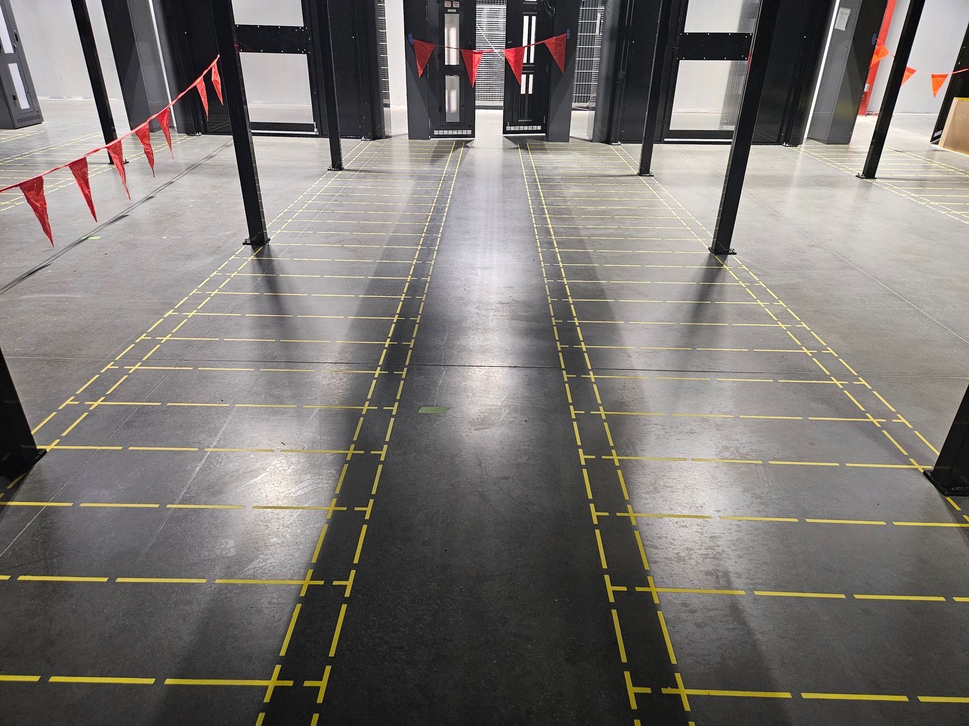 Interior view of a training facility with a dark floor, marked lanes, and black support columns.