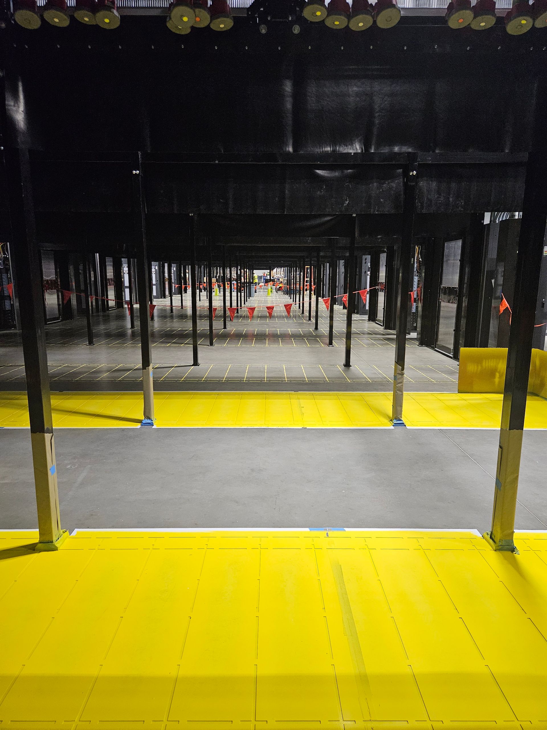 Yellow and gray warehouse floor with black supports, white targets in the distance, and overhead lighting.