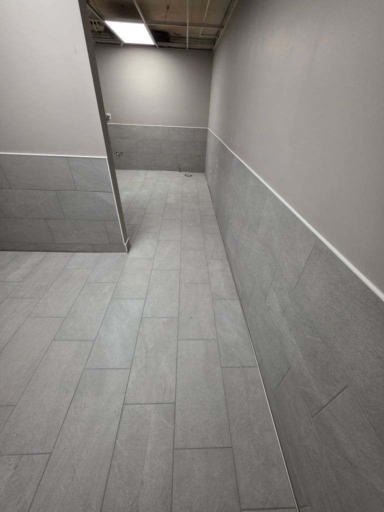Gray tiled floor and walls with a white trim in a hallway.