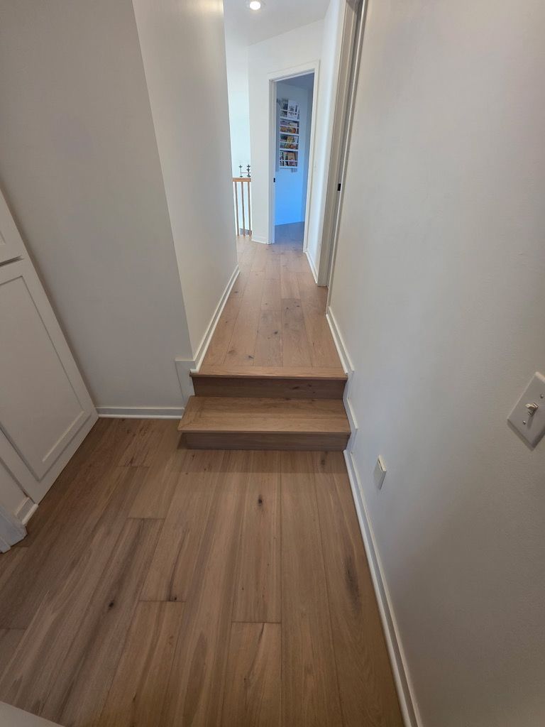Hallway with wood floors and stairs leading to a doorway, white walls, and trim.