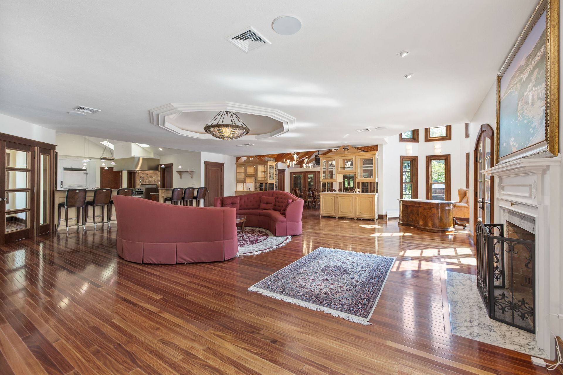 Spacious living room with hardwood floors, red curved sofa, fireplace, and open kitchen in background.
