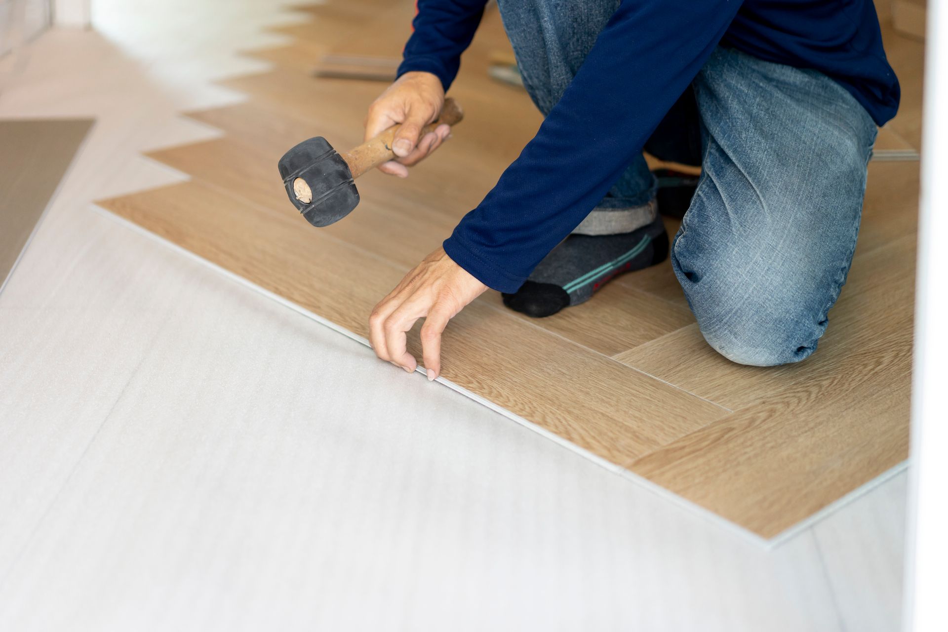 Person installing wood-look flooring, using a hammer to secure planks.