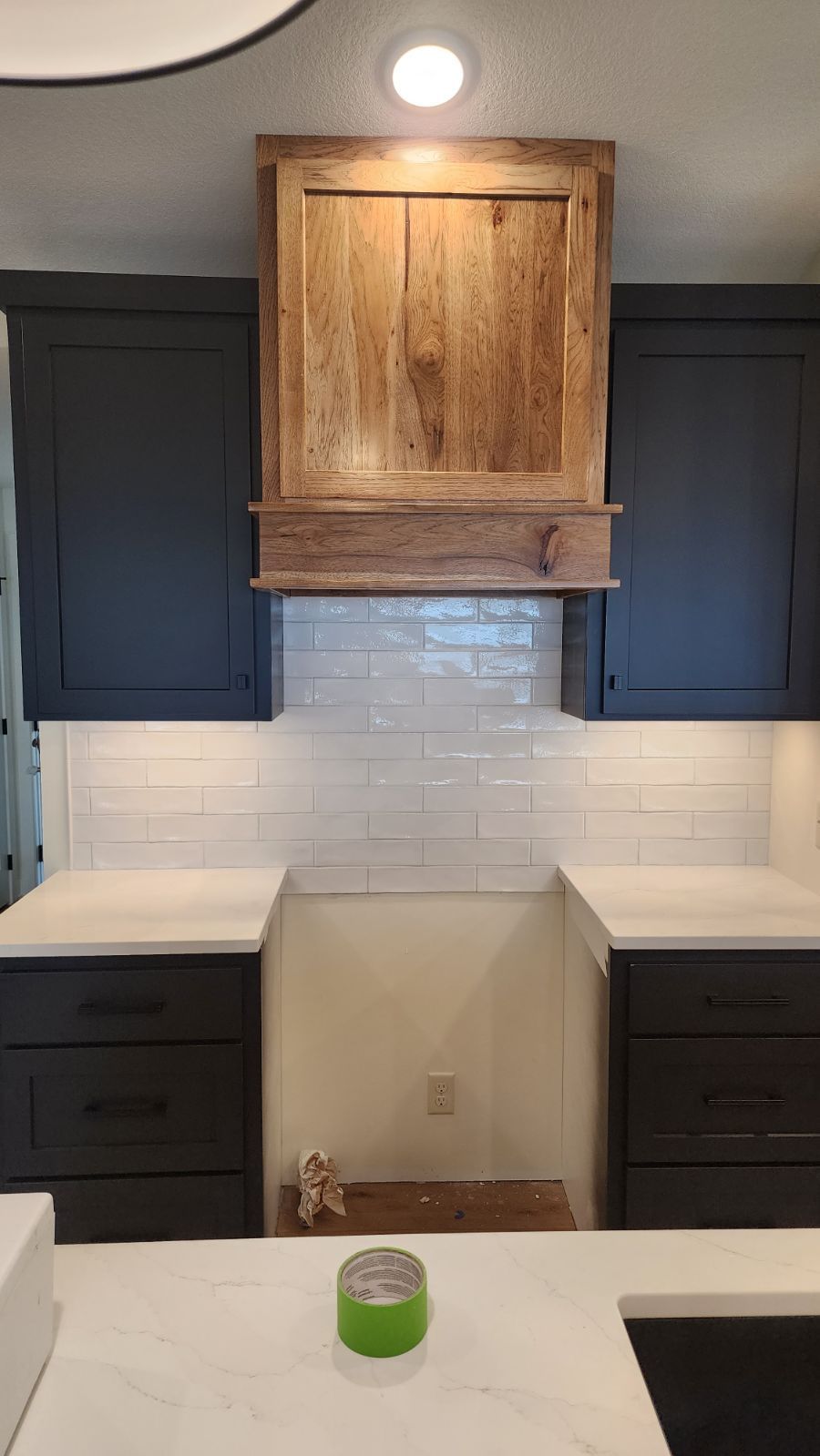 Kitchen with dark cabinets, white countertops, and wood range hood.